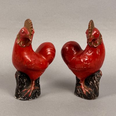 pair of red rooster figurines sitting on top of a tree stump