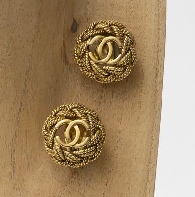two pairs of gold toned chanel earrings on a wooden stand