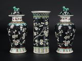 trois vases noirs ornés de fleurs et d'oiseaux, posés sur un fond noir