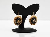 a pair of black and gold earrings on a black stand