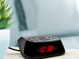 a black alarm clock sitting on a table next to a potted plant