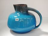 un vase bleu muni d'une anse marron posé sur une table