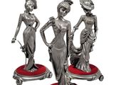 three silver figurines of women on red pedestals on a white background