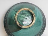 a green vase with a gold rim sitting on a white surface