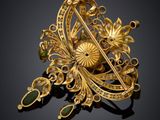 a gold broochle with green stones on a black background