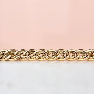un gros plan d'un bracelet à chaîne dorée sur fond rose