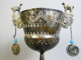 a silver vase with a blue bead hanging from it ' s handle