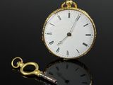 une montre de poche en or avec une clé, sur un fond noir