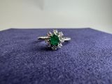 a close up of a ring with a green stone surrounded by white diamonds