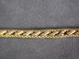 a close up of a gold braided bracelet on a gray surface