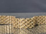 gold tone bracelet on a shiny surface with a black background