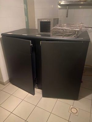 two black refrigerators in a small kitchen with a sink
