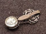 une pince à cravate en argent sur laquelle est fixée une montre de poche