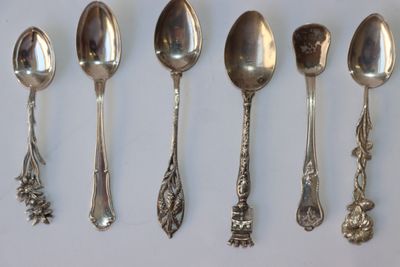 six cuillères en argent sont alignées sur une surface blanche