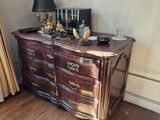 une commode placée dans un coin de la pièce, sur laquelle est posée une lampe