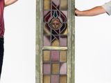 two men standing next to a tall stained glass window with a face on it