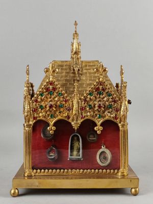 une horloge dorée et rouge posée sur un socle, sur une surface blanche