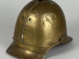 un vieux casque en laiton posé sur une surface blanche, avec un fond gris