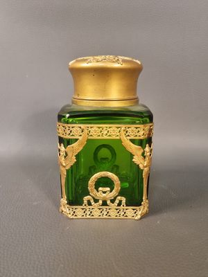 un bocal en verre vert avec un couvercle doré sur lequel figure une image