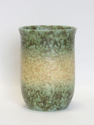 a green and yellow vase sitting on a white surface