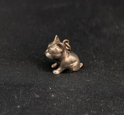 une petite breloque en forme de chien en argent posée sur un tissu noir