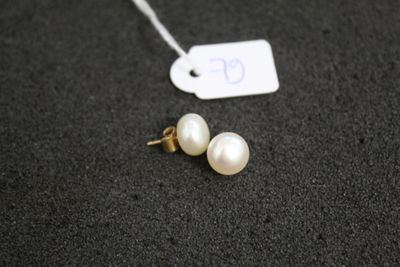 une paire de boucles d'oreilles en perles blanches posées sur un fond noir, avec une étiquette de prix