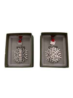 two silver snowflake ornaments in a box on a white background