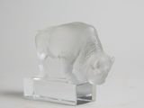 une figurine en verre représentant un bison blanc, posée sur un socle transparent