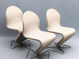 three white chairs sitting on top of each other in front of a gray wall