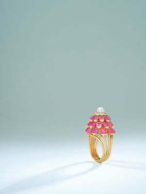 a gold ring with pink stones and pearls on a white surface