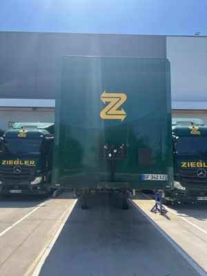 plusieurs gros camions verts garés sur un parking, avec une personne assise par terre