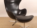 une photo d'un fauteuil « œuf » en cuir noir et d'un repose-pieds dans un salon
