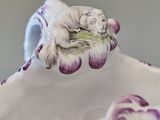 a white and purple vase with a cat sitting on top of it
