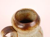 a brown and white vase with a handle on a table