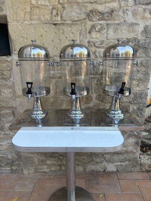 three drinks dispensers sitting on a table in front of a stone wall