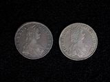 two silver coins on a black surface with one of them facing the camera