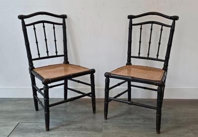 une paire de chaises noires avec des assises en osier, posées contre un mur blanc