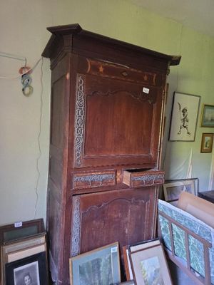 une grande armoire en bois dans une pièce où sont accrochés des tableaux au mur