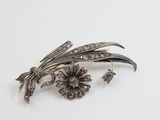 a silver brooch with flowers on it on a white surface