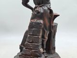 bronze figurine of a man sitting on a rock holding a bottle of wine