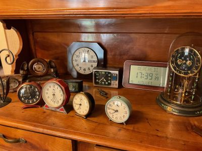 many different clocks on a wooden shelf in a room