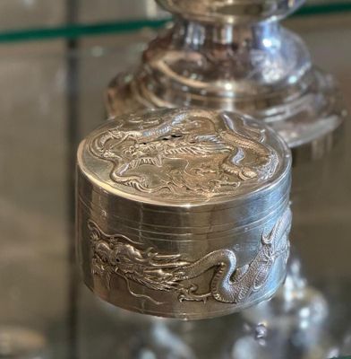 a silver box with a dragon on it sitting on a glass shelf