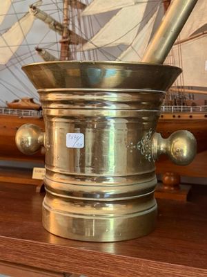 a brass mortar and a wooden model of a ship in the background