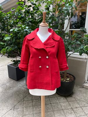 un manteau en laine rouge posé sur un mannequin devant une plante en pot