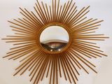 un miroir doré à rayons de soleil sur un mur blanc, avec un miroir au milieu