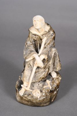 an old figurine of a man sitting on a rock with a stick