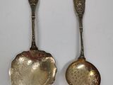 two silver spoons with ornate designs on them sitting next to each other