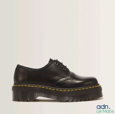 chaussures Dr Martens noires avec des lacets jaunes sur fond blanc