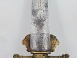 a close up of a gold and silver sword on a wooden stand