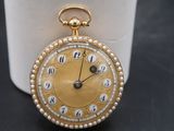 a gold pocket watch sitting on a table next to a cup
